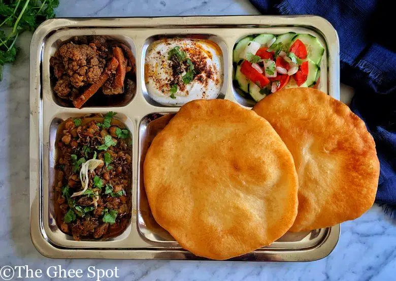 Tangy, savory, and spicy, Amritsari chole with bhatura, raita, salad, and achar
